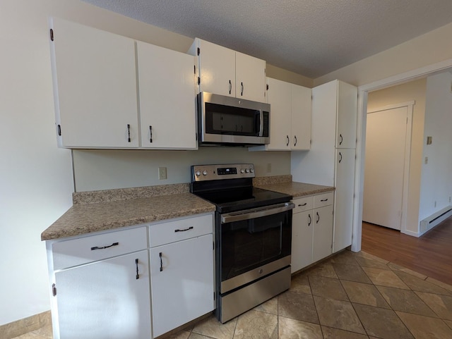 kitchen with a textured ceiling, light tile patterned floors, a baseboard radiator, appliances with stainless steel finishes, and white cabinets