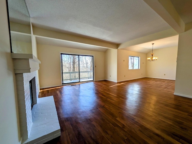 unfurnished living room with a brick fireplace, dark wood-type flooring, a chandelier, and a healthy amount of sunlight