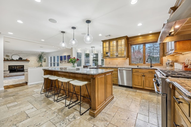 kitchen featuring brown cabinets, stainless steel appliances, stone tile flooring, ventilation hood, and a kitchen breakfast bar