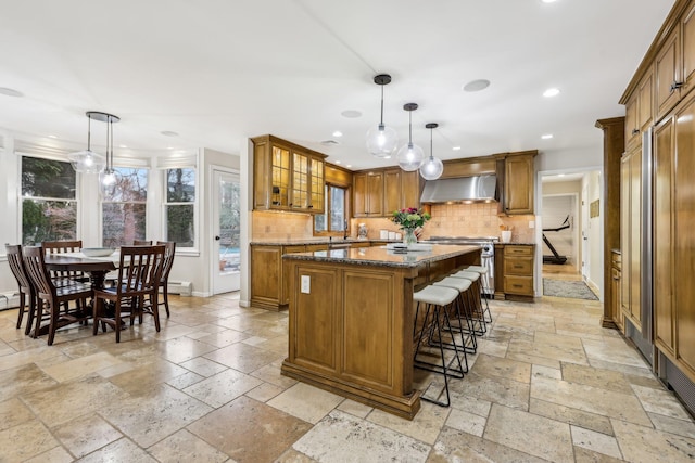 kitchen featuring stone tile floors, brown cabinetry, a center island, stainless steel stove, and wall chimney range hood