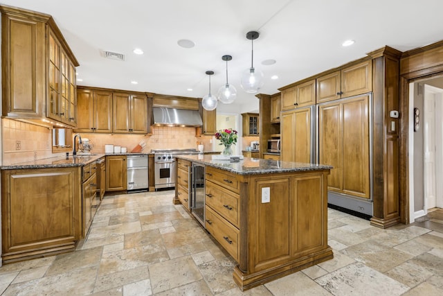 kitchen with premium appliances, brown cabinets, wall chimney range hood, and stone tile floors