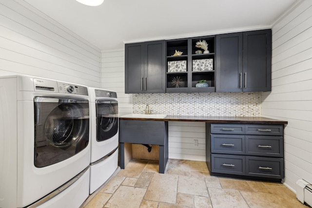 clothes washing area with a baseboard radiator, stone tile floors, a sink, cabinet space, and washing machine and clothes dryer