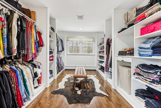 walk in closet with visible vents, a baseboard heating unit, and wood finished floors