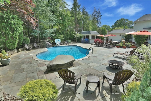 outdoor pool featuring a fire pit, an outbuilding, and a patio