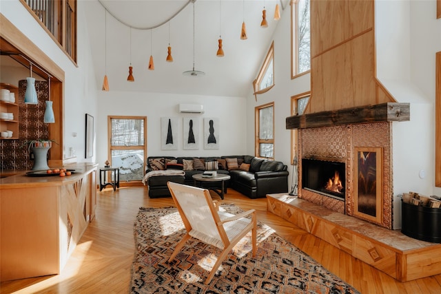 living room with a towering ceiling, a fireplace, a wall mounted AC, and light hardwood / wood-style flooring