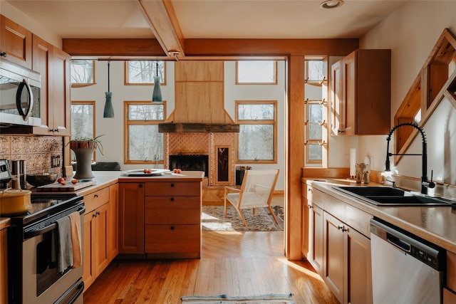 kitchen with sink, beam ceiling, stainless steel appliances, and light wood-type flooring