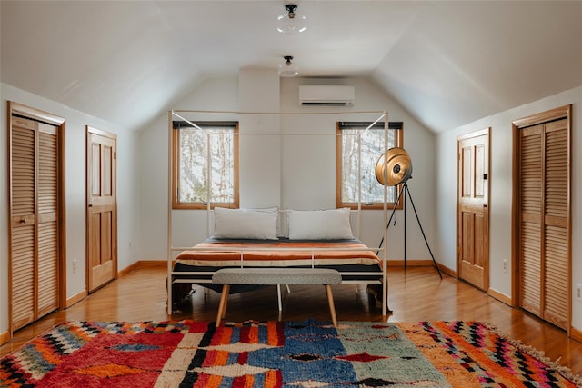 bedroom featuring multiple closets, vaulted ceiling, an AC wall unit, and light wood-type flooring