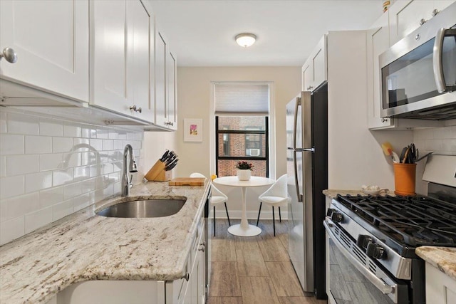 kitchen with sink, white cabinetry, appliances with stainless steel finishes, light stone countertops, and decorative backsplash