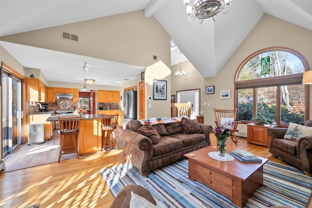 living room with light hardwood / wood-style flooring, a notable chandelier, high vaulted ceiling, beamed ceiling, and sink