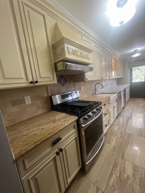 kitchen with light stone counters, backsplash, cream cabinets, appliances with stainless steel finishes, and a sink