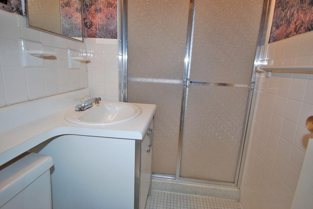 bathroom with vanity, toilet, a shower with shower door, and tile walls