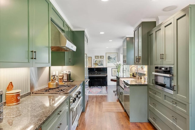 kitchen featuring light stone counters, green cabinetry, crown molding, light wood-type flooring, and appliances with stainless steel finishes