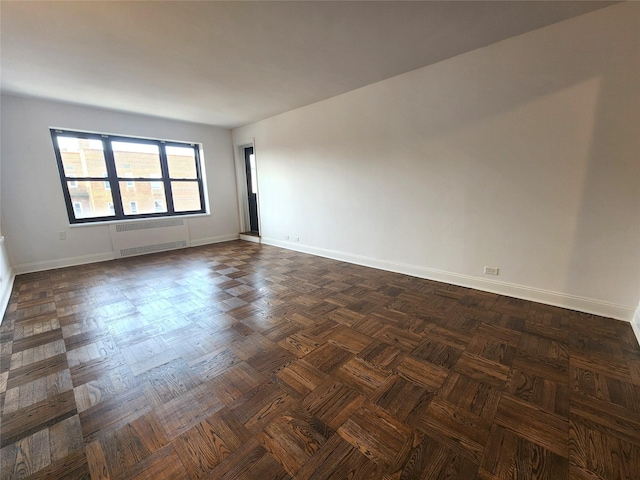 empty room featuring dark parquet flooring and radiator heating unit