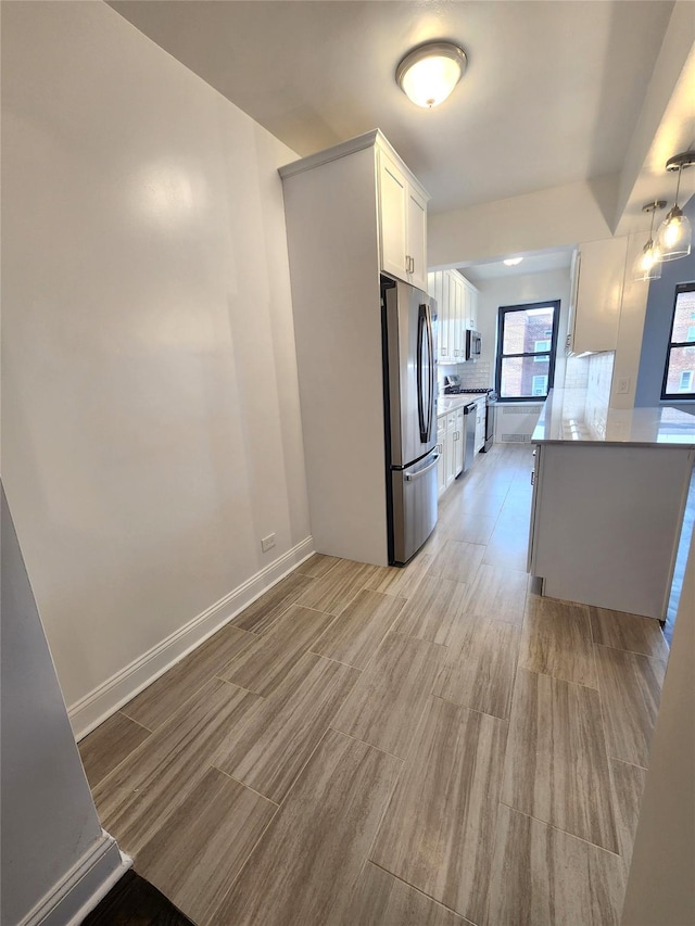 kitchen with tasteful backsplash, appliances with stainless steel finishes, hanging light fixtures, and white cabinets