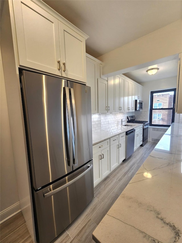 kitchen featuring radiator, appliances with stainless steel finishes, light stone countertops, white cabinets, and decorative backsplash