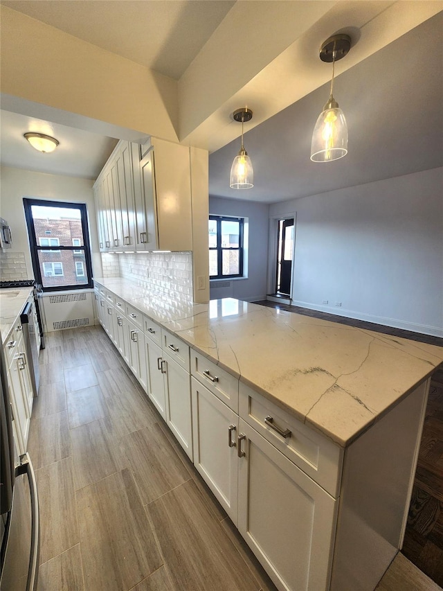 kitchen with light stone counters, white cabinetry, decorative light fixtures, radiator, and decorative backsplash