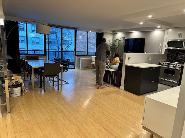 kitchen with backsplash, a wall of windows, stainless steel appliances, and light hardwood / wood-style floors