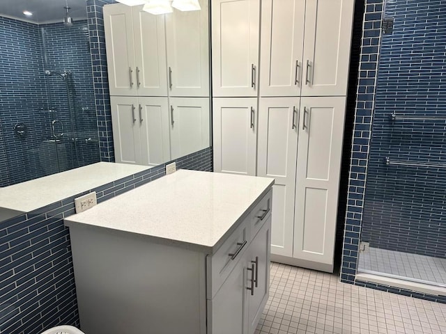 bathroom featuring vanity, a tile shower, tile patterned floors, and tile walls