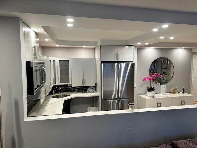 kitchen featuring sink, white cabinetry, kitchen peninsula, stainless steel appliances, and decorative backsplash