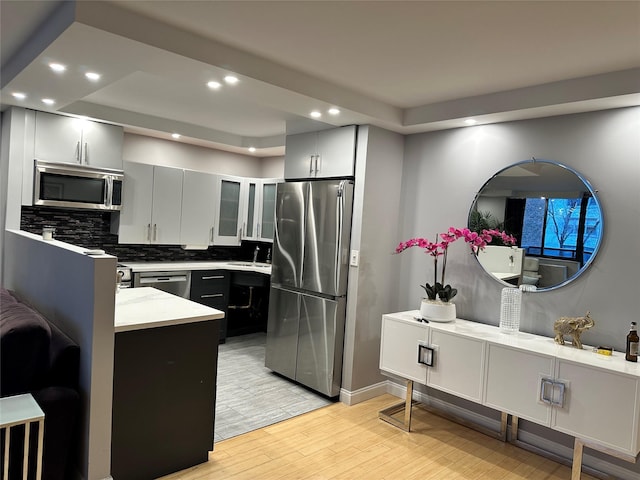 kitchen with appliances with stainless steel finishes, tasteful backsplash, sink, light stone countertops, and light hardwood / wood-style flooring