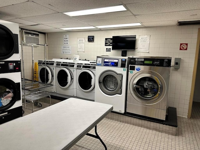 laundry room featuring separate washer and dryer, tile walls, stacked washer and clothes dryer, light tile patterned floors, and a wall unit AC