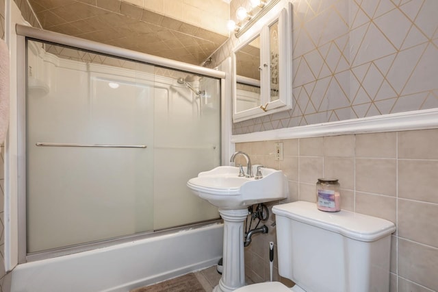 bathroom featuring tile walls, shower / bath combination with glass door, and toilet