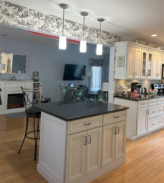 kitchen with decorative light fixtures, white cabinetry, a breakfast bar area, a center island, and light hardwood / wood-style flooring