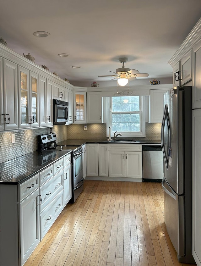 kitchen with sink, light hardwood / wood-style flooring, appliances with stainless steel finishes, backsplash, and white cabinets