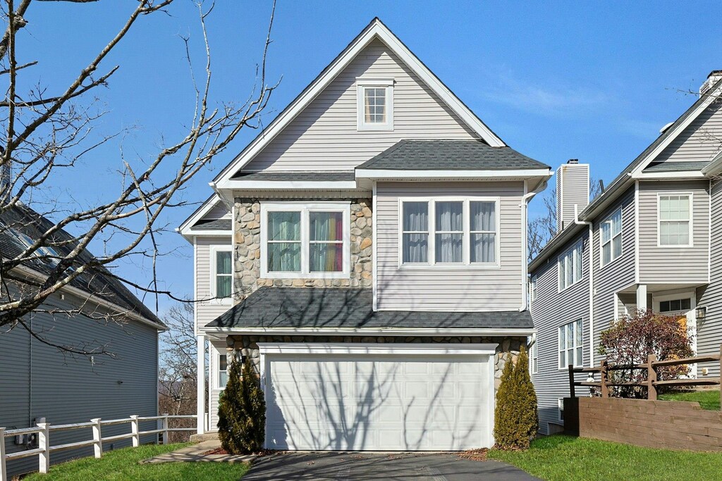 view of front of property with an attached garage, fence, stone siding, and driveway