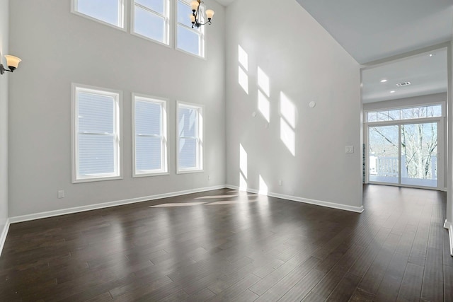 unfurnished living room with visible vents, a notable chandelier, baseboards, a towering ceiling, and dark wood-style flooring