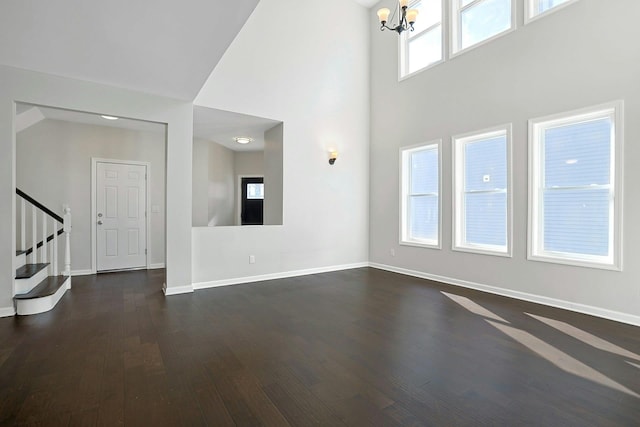 unfurnished living room with a notable chandelier, dark wood-style floors, baseboards, a towering ceiling, and stairs