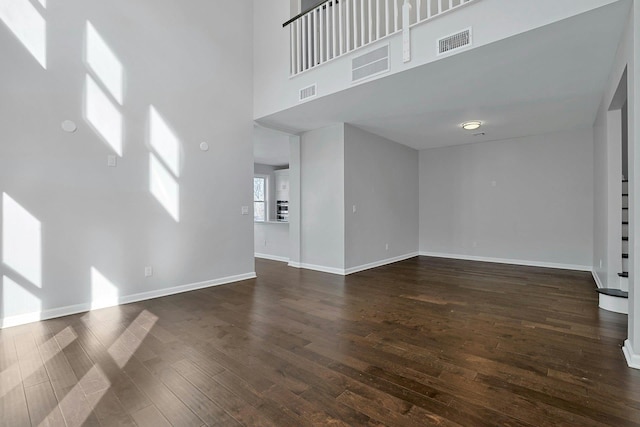 unfurnished living room with visible vents, baseboards, dark wood-style floors, and a towering ceiling