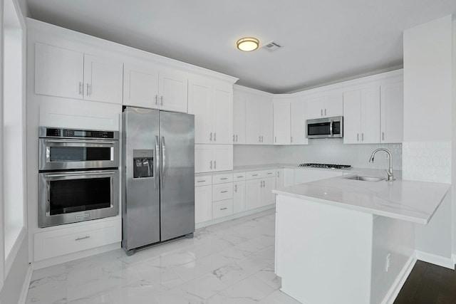 kitchen featuring visible vents, a peninsula, a sink, stainless steel appliances, and marble finish floor