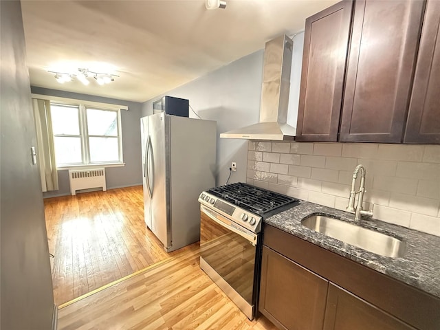 kitchen with sink, dark stone countertops, radiator, stainless steel appliances, and wall chimney range hood