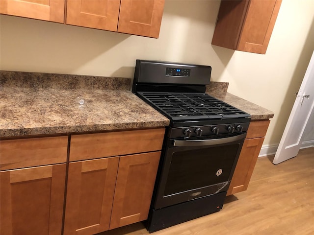 kitchen featuring light wood-type flooring, gas stove, and dark stone countertops