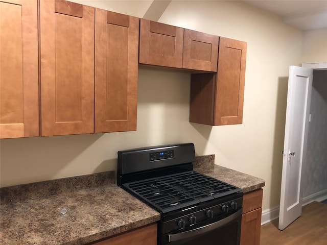 kitchen with black gas range, hardwood / wood-style flooring, and dark stone countertops