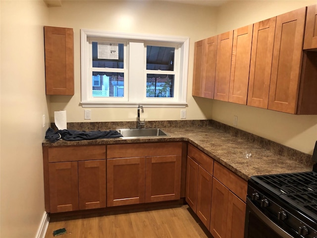 kitchen with black range with gas stovetop, light hardwood / wood-style floors, sink, and dark stone countertops