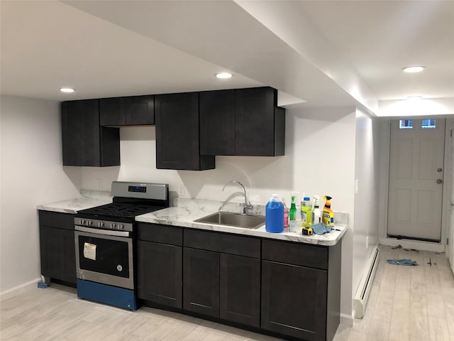 kitchen with stainless steel gas stove, sink, a baseboard heating unit, light stone countertops, and light wood-type flooring