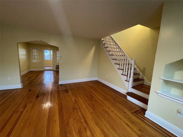 64-18 84th Pl, Middle Village, NY 11379 - unfurnished living room featuring wood finished floors, stairs, arched walkways, and baseboards