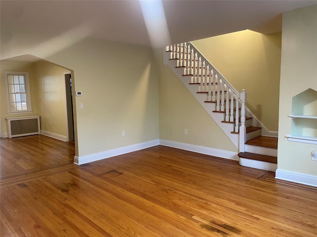 64-18 84th Pl, Middle Village, NY 11379 - unfurnished living room with radiator, hardwood / wood-style floors, stairway, lofted ceiling, and baseboards