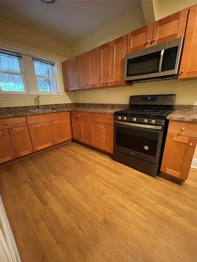 64-18 84th Pl, Middle Village, NY 11379 - kitchen with appliances with stainless steel finishes, light wood finished floors, a sink, brown cabinetry, and dark countertops