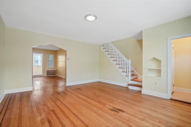 64-18 84th Pl, Middle Village, NY 11379 - unfurnished living room with radiator heating unit, arched walkways, light wood-style floors, stairs, and built in shelves