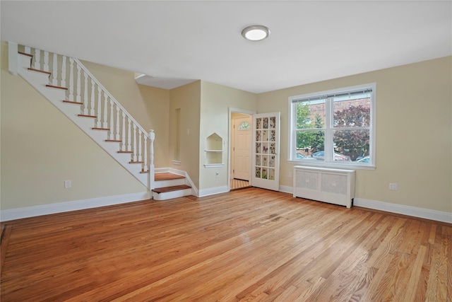 64-18 84th Pl, Middle Village, NY 11379 - unfurnished living room with radiator, light wood-style floors, and stairway