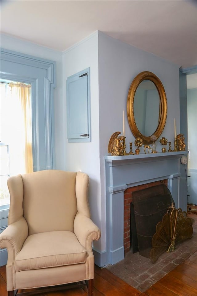 living area with hardwood / wood-style flooring, ornamental molding, and a brick fireplace