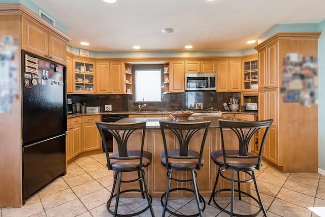 kitchen with a center island, black appliances, light tile patterned flooring, decorative backsplash, and light brown cabinets