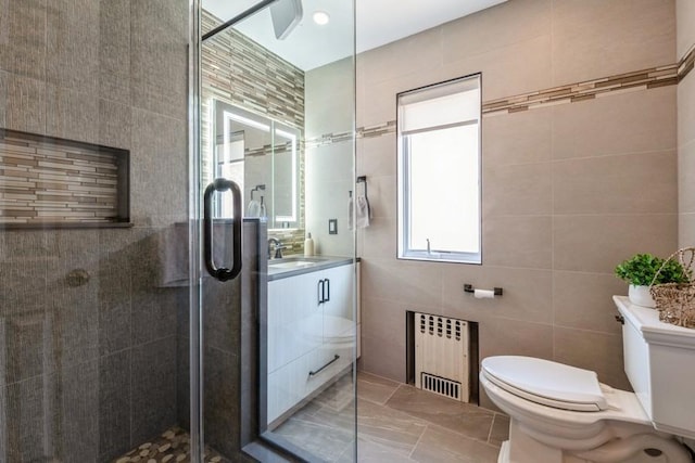 bathroom featuring radiator, tile walls, vanity, an enclosed shower, and toilet