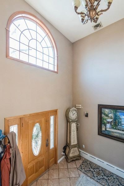 foyer featuring light tile patterned floors, a baseboard radiator, a chandelier, and a high ceiling