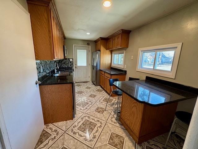 kitchen with sink, a breakfast bar area, stainless steel fridge, backsplash, and kitchen peninsula