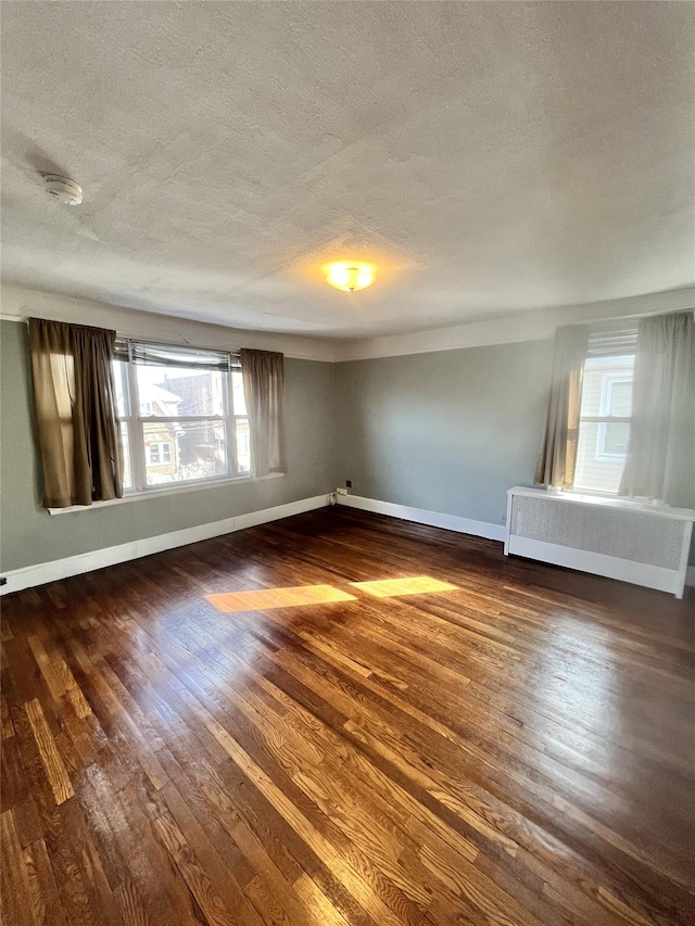 empty room with radiator heating unit, a textured ceiling, and dark hardwood / wood-style flooring