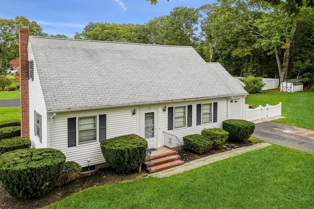 cape cod house featuring an outbuilding, a storage shed, driveway, a chimney, and a front yard